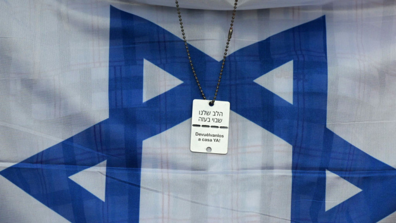Una medalla con la leyenda "Envíenlos de regreso a casa ahora" se ve frente a una bandera israelí mientras la gente marcha exigiendo la liberación de todos los rehenes restantes retenidos en Gaza desde el ataque de Hamás del 7 de octubre de 2023 contra Israel, durante una manifestación convocada por la comunidad judía en Buenos Aires el 24 de febrero de 2025. (Juan Mabromata / AFP vía Getty Images)