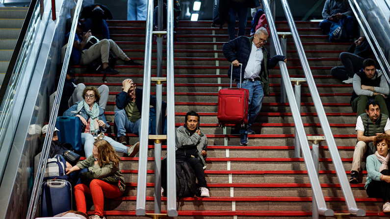 Los viajeros se sientan en las escaleras mientras se preparan para pasar la noche en la estación de tren de Atocha, tras un apagón masivo que ha afectado a toda la península ibérica y al sur de Francia, en Madrid, el 28 de abril de 2025. (Foto de OSCAR DEL POZO/AFP a través de Getty Images)
