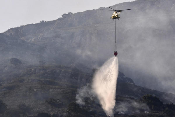 Un helicóptero trabaja en las labores de extinción del incendio que desde ayer afecta a la Sierra de la Plata, en Tarifa, Cádiz. (EFE/Román Ríos)