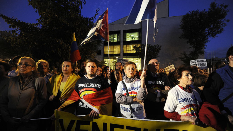 Miembros de la Asociación de Víctimas del Terrorismo (AVT) llevan camisetas con la leyenda "Romper el silencio, por ellos, por todos", pancartas con la leyenda "Chávez nos humilla. ¿Se doblega España?" y ondean banderas mientras protestan frente a la embajada de Venezuela el 14 de octubre de 2010 en Madrid.  AFP PHOTO/ JAVIER SORIANO (Crédito de la foto: JAVIER SORIANO/AFP vía Getty Images)