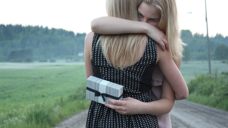 Dos mujeres se abrazan fraternalmente mientras que una de ellas sostiene un regalo en su mano izquierda. Moilanen. Pixabay