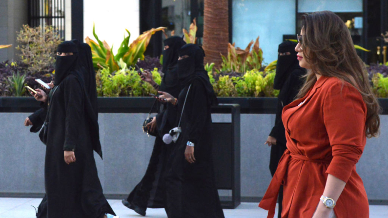 Imagen ilustrativa. Una mujer camina vestida con ropa occidental junto a mujeres que llevan niqab, la vestimenta islámica femenina, en una zona comercial de Riad, la capital saudí, el 3 de septiembre de 2019. (FAYEZ NURELDINE/AFP vía Getty Images)